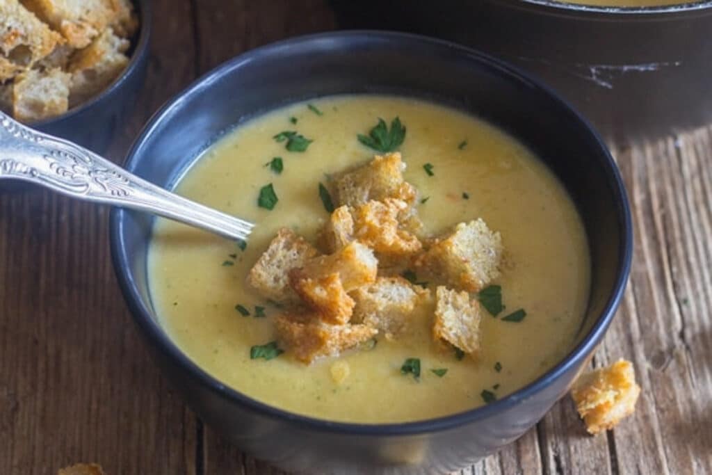 Squash soup in a black bowl with a silver spoon.