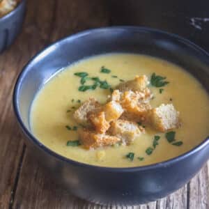Squash soup in a black bowl with croutons on top.