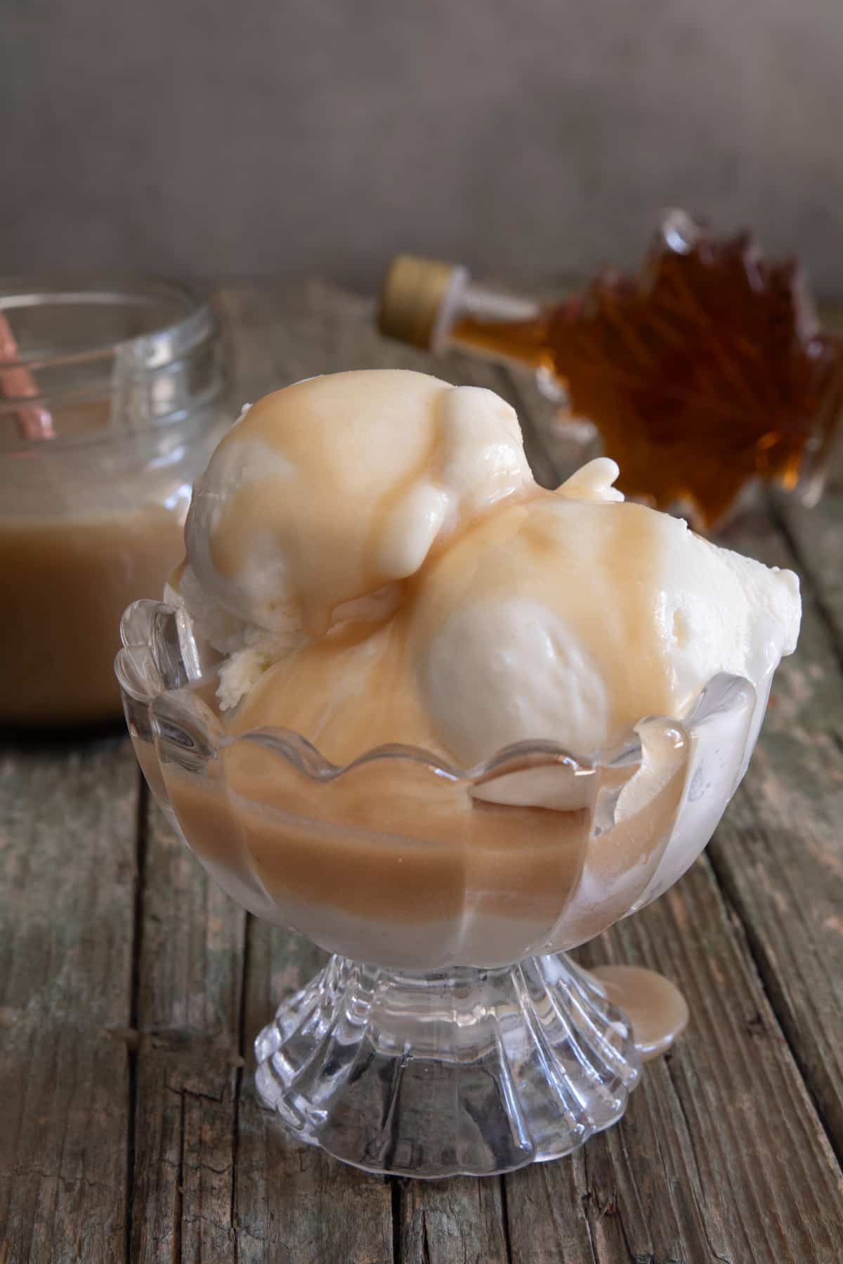 Caramel sauce on three scoops of vanilla ice cream in a glass bowl.