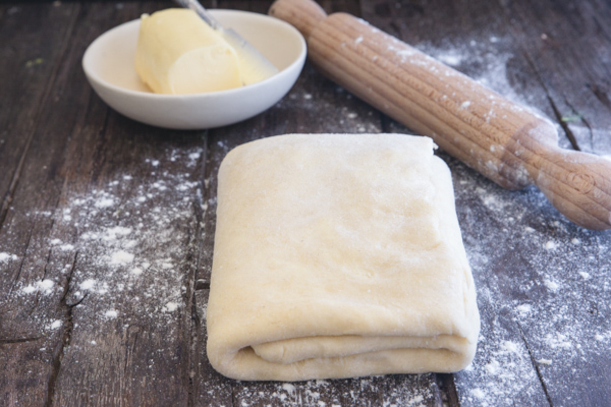 Puff pastry folded on a wooden board with a rolling pin.