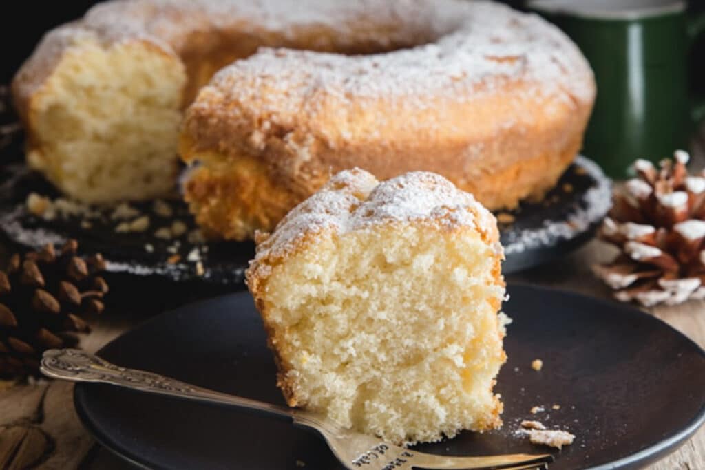 Cake on a wire rack with a slice on a black plate with a fork.