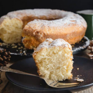 Cake on a wire rack with a slice on a black plate with a fork.