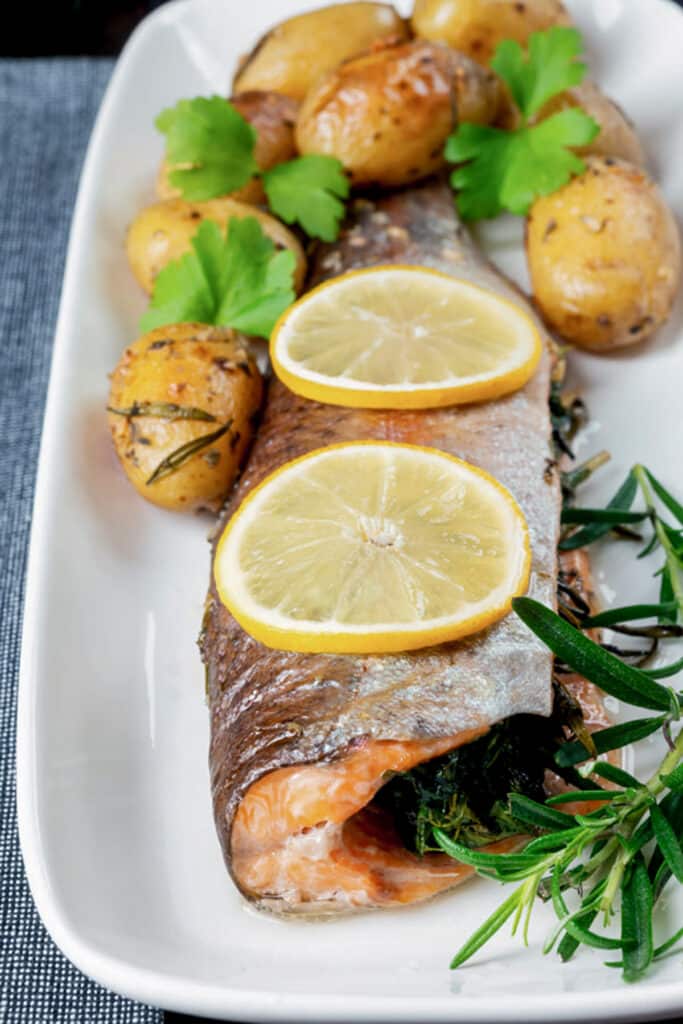 Trout on a white dish with lemon slices and potatoes.