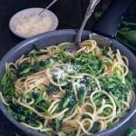 Pasta and broccoletti in a black pan with a silver fork.