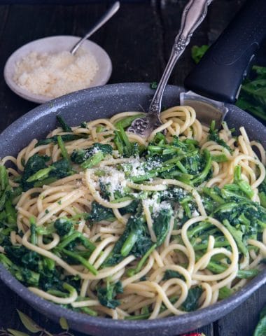 Pasta and broccoletti in a black pan with a silver fork.