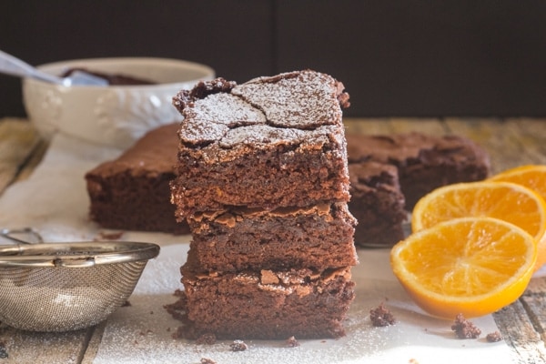 Schokoladen-Orangen-Brownies auf einem Holzbrett mit 3 Orangenscheiben und Puderzucker