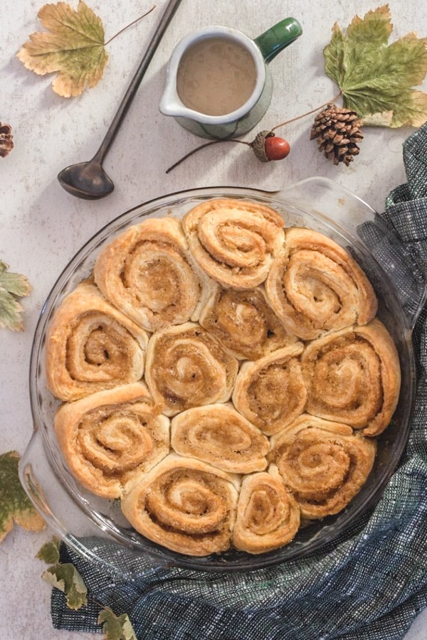 cinnamon rolls in the pie plate with maple glaze in a jar