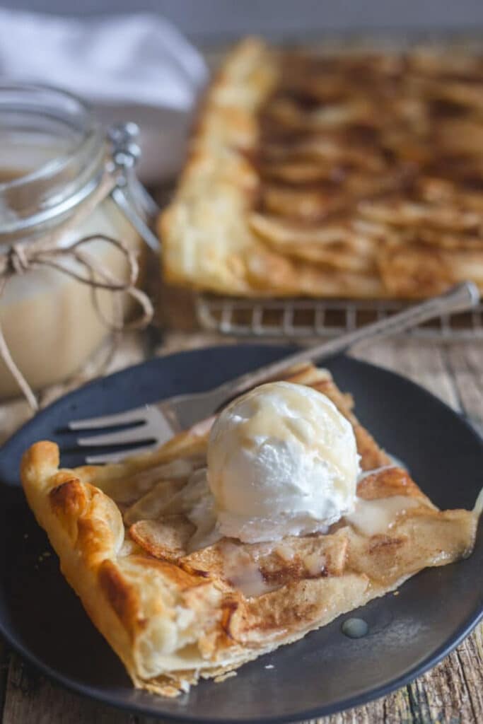 Cinnamon apple tart on a wire rack with a slice on a black plate.