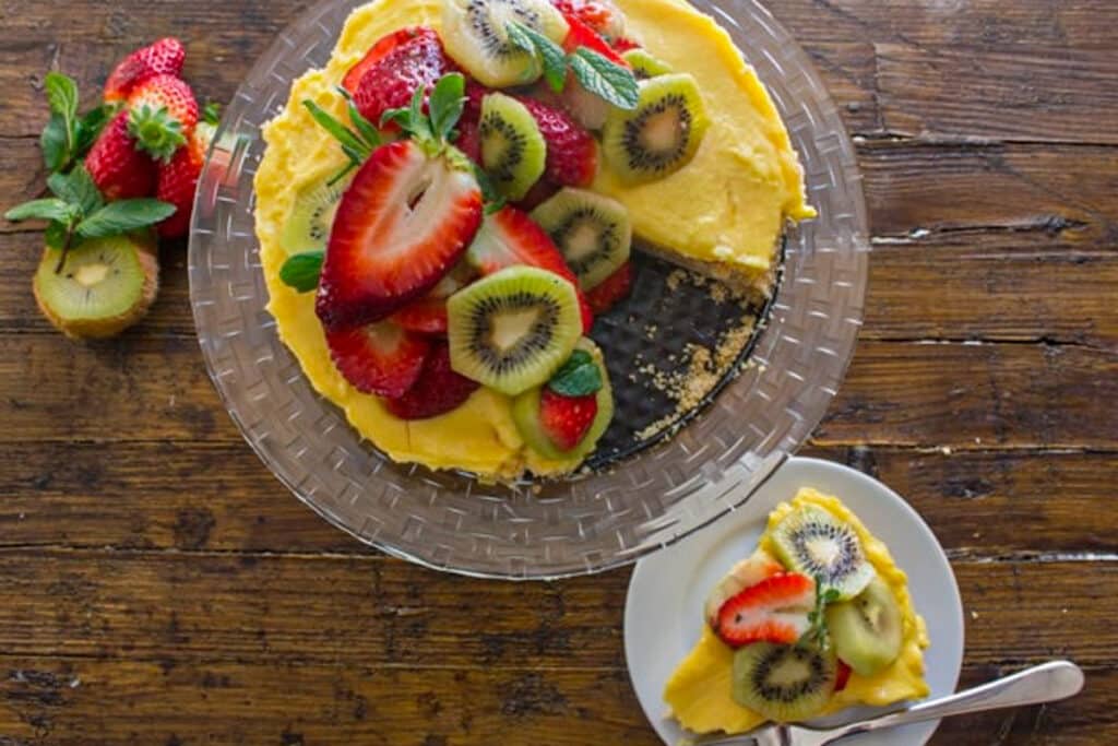 Fruit tart on a glass plate and a slice on a white plate.
