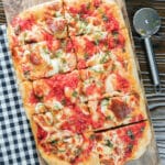 Pizza on a wooden board cut into pieces.