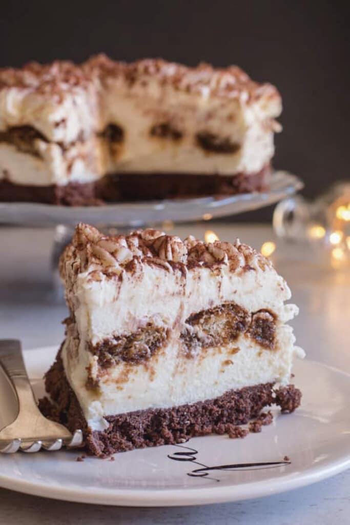 Tiramisu cheesecake on a glass cake stand with a slice on a white plate.