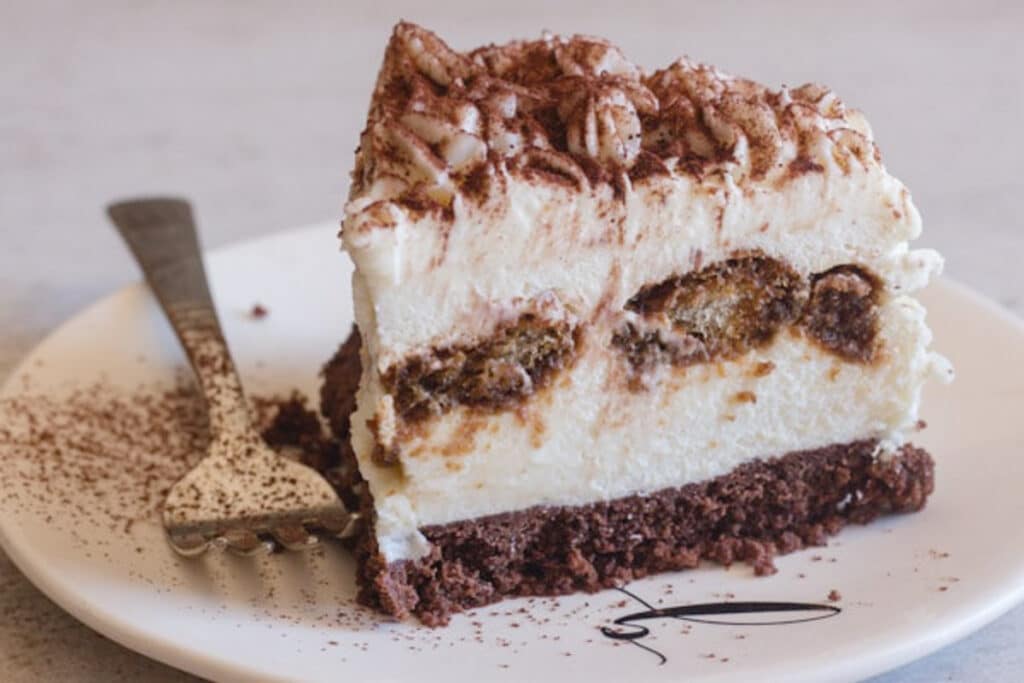 A slice of cheesecake on a white dish with a fork.