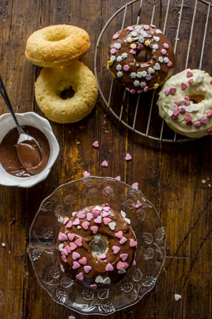 Chocolate glazed vanilla donuts on a wire rack and on a plate and wooden board.