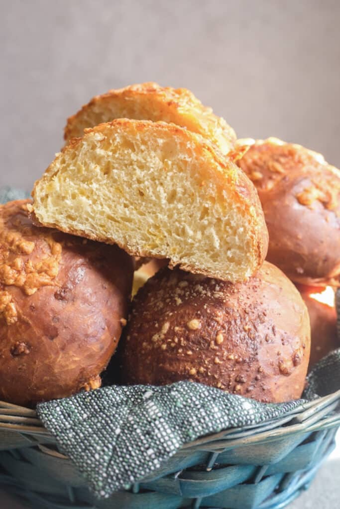 Cheese buns in a basket with one cut in half.