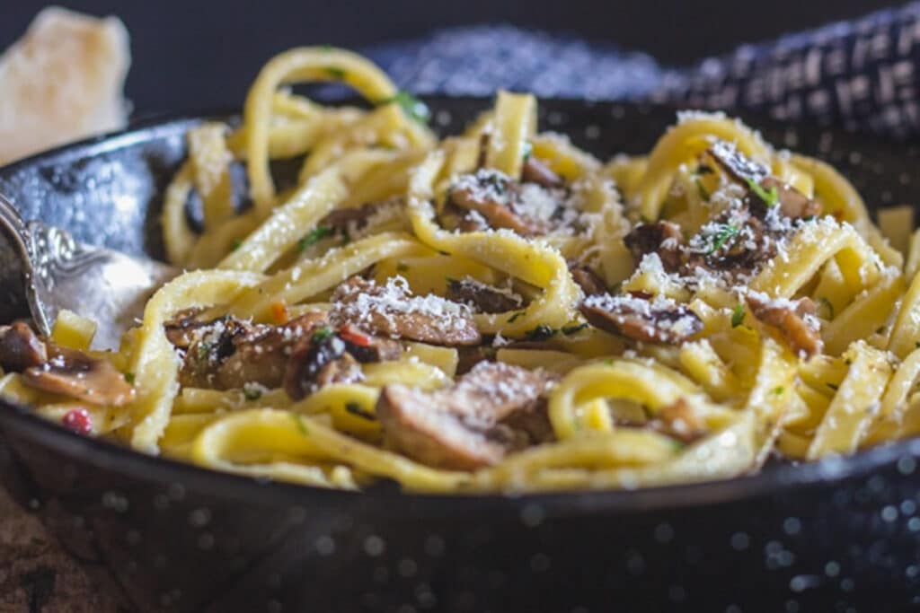 Pasta in a black pan with cheese on top.