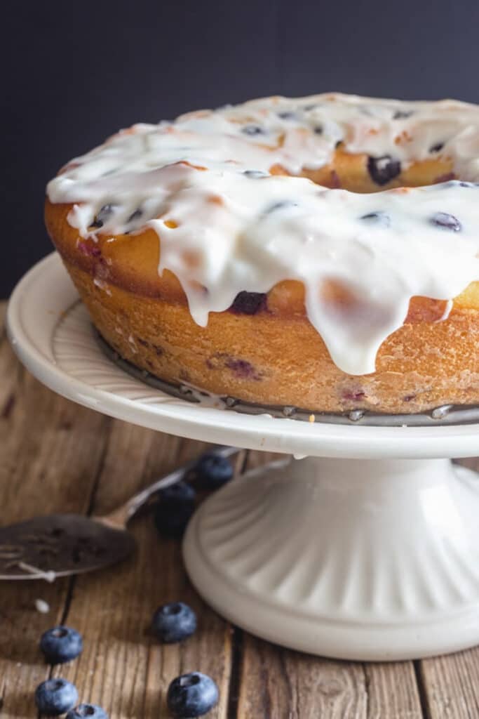 Blueberry cake with glaze on a white cake stand.