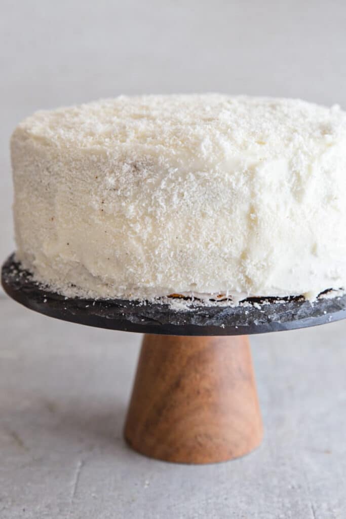 Coconut cake on a black wood cake stand.