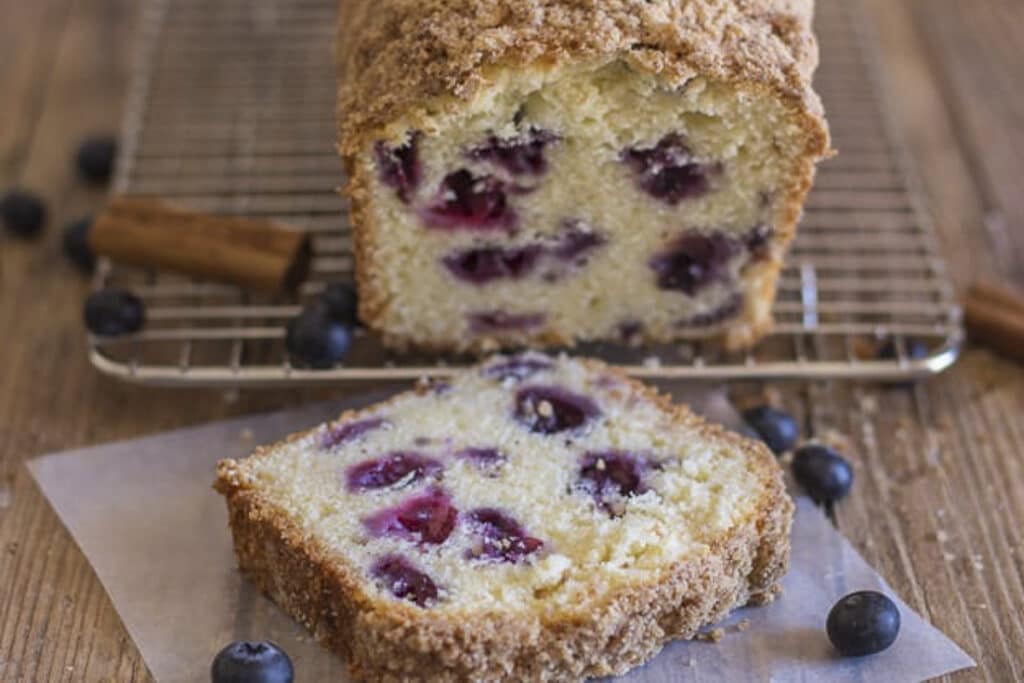 Blueberry bread with a slice cut on a wire rack.