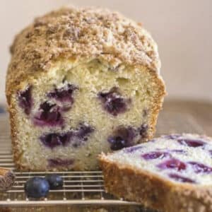 Blueberry bread with a slice cut on a wire rack.