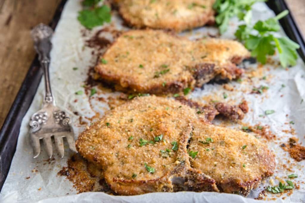 Pork chops on parchment paper lined baking sheet.
