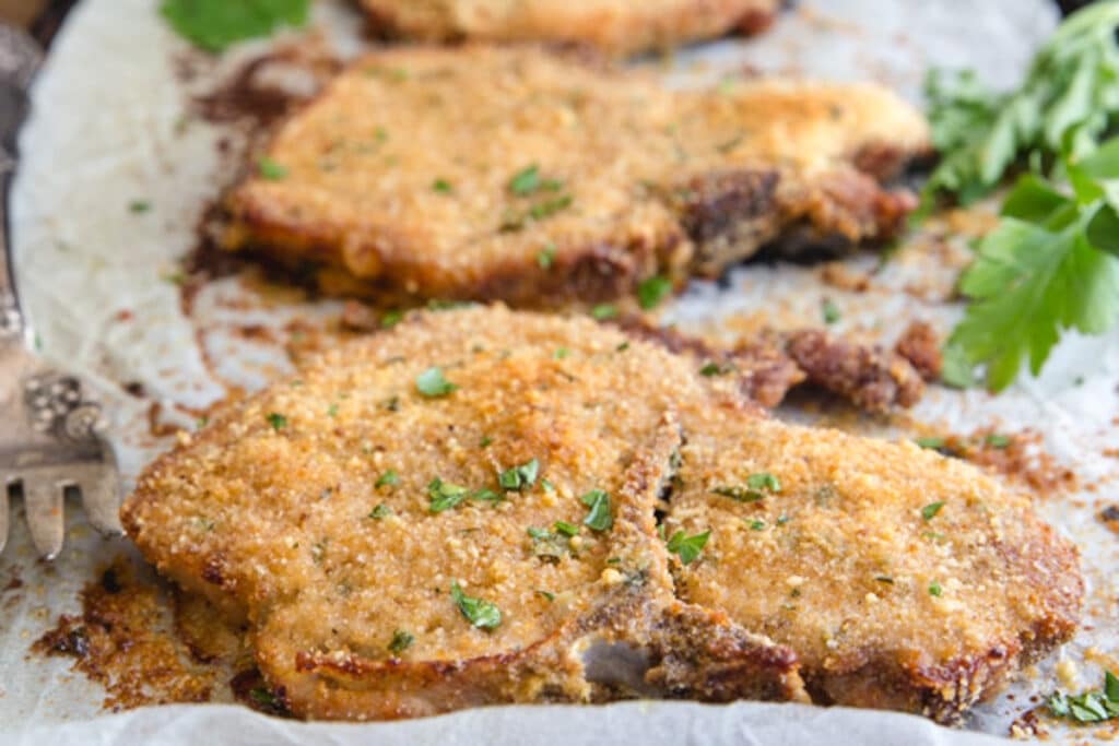 Pork chops on parchment paper lined baking sheet.