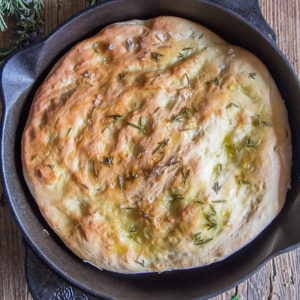 Focaccia bread in a black skillet with chopped rosemary.