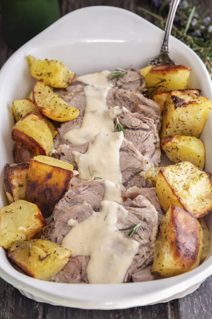 Roast beef with gravy and potatoes in a white dish.