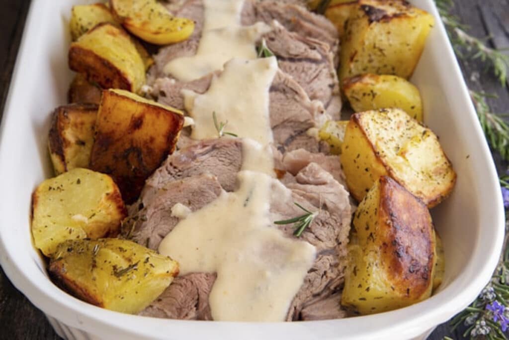 Roast beef with gravy and potatoes in a white dish.