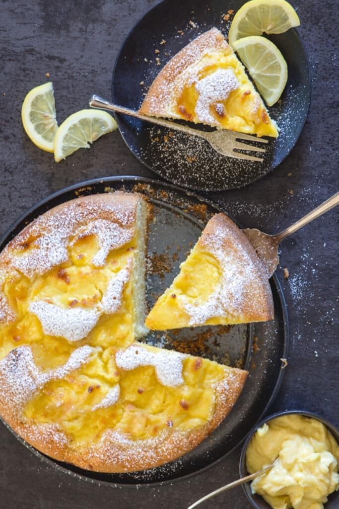 Lemon cake on a black plate with a slice on a small black plate.