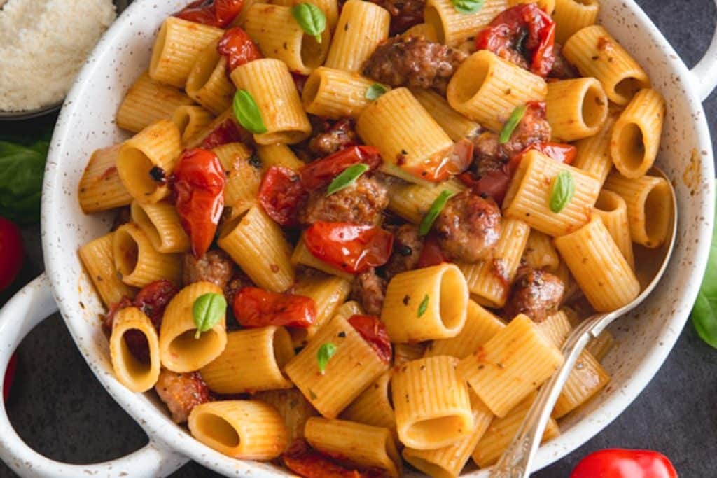 Sausage pasta in a white dish with a silver serving spoon.