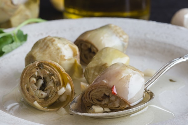 up close baby artichokes under oil on a white plate