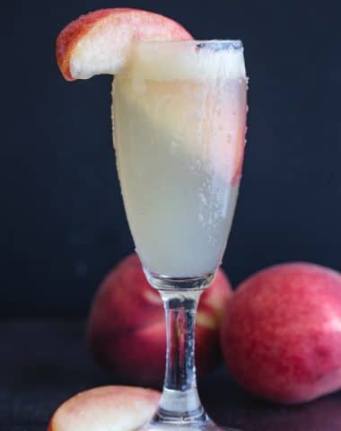 bellini cocktail in a flute glass with a slice of peach