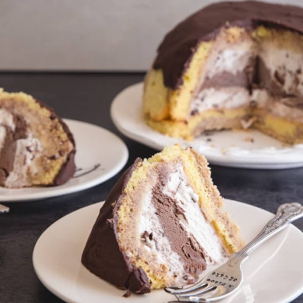 Ice cream cake on a white plate with two slices cut on white plates.