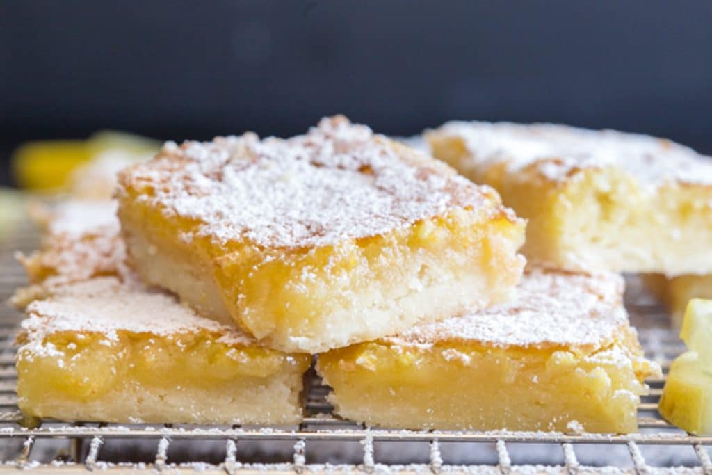 Lemon squares on a wire rack with one on top.