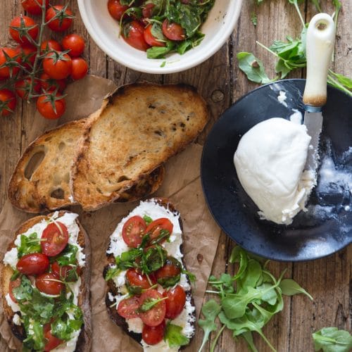 burrata bruschetta on a brown paper with fresh tomatoes