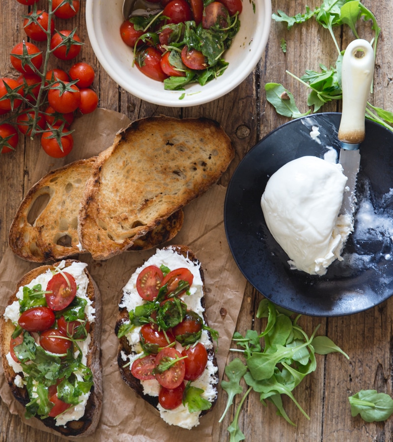 burrata bruschetta on a brown paper with fresh tomatoes