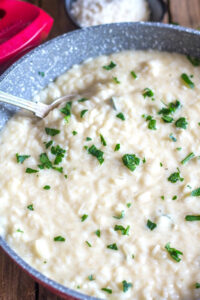 Risotto in a red pan with a silver spoon.