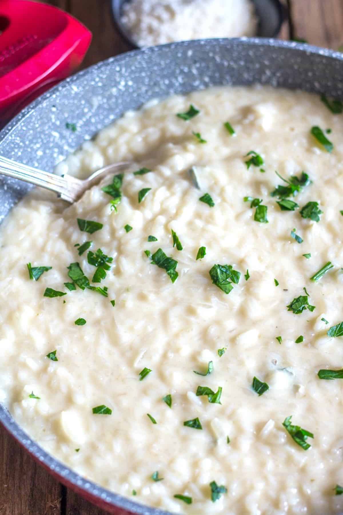 Risotto in a red pan with a silver spoon.