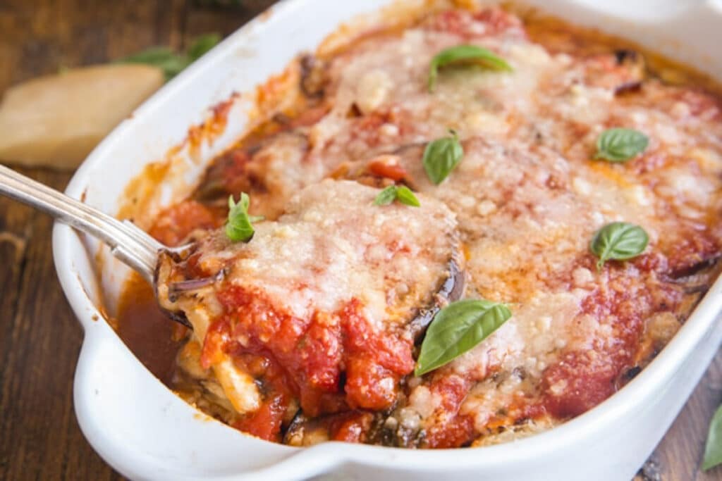 Eggplant parmesan in a white baking dish with some on a spoon.