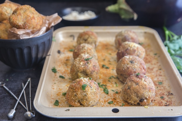 eggplant meatballs baked on a cookie sheet with fried meatballs in a black bowl
