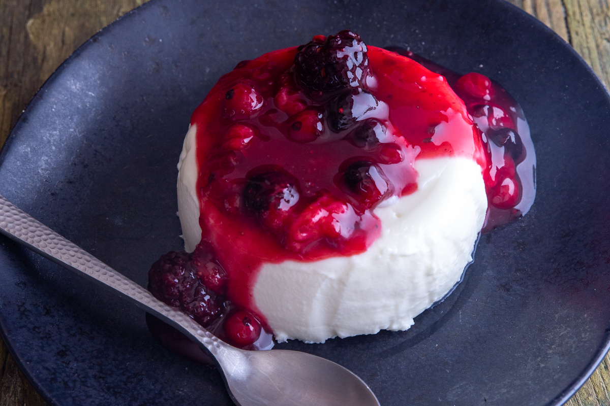 Panna cotta on a black plate with a silver spoon.