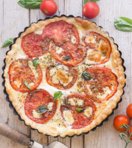 Tomato pie on a white board, with a serving spatula.