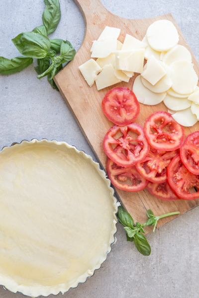 The crust in the pie plate & the cheese & tomatoes sliced on a board.