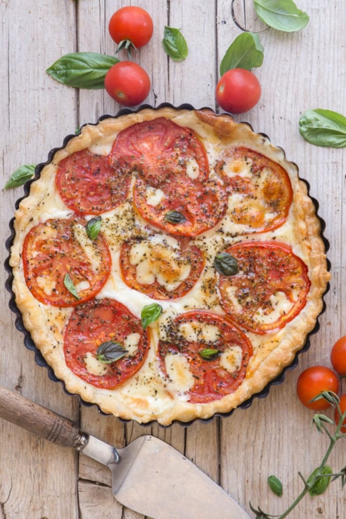 Tomato pie on a white board, with a serving spatula.