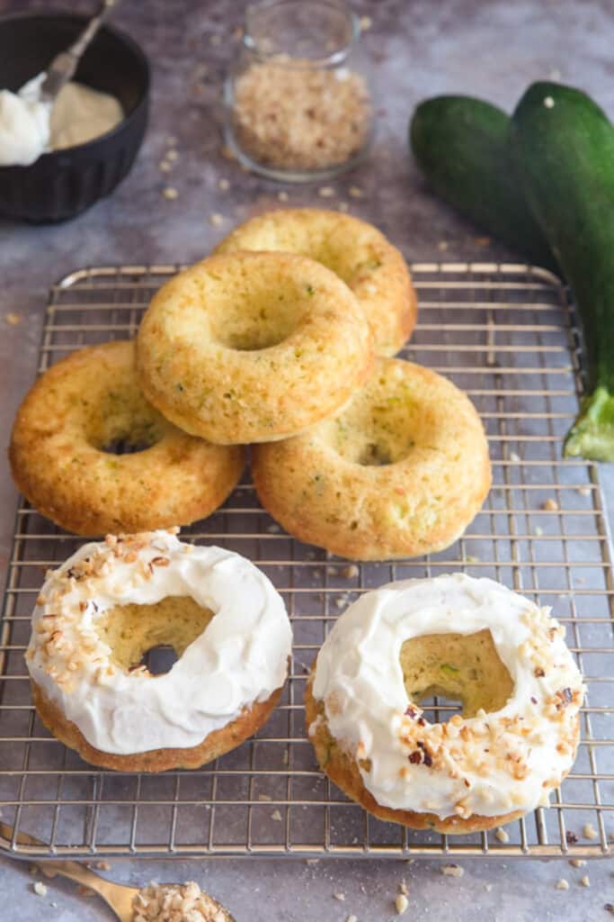 Zucchini donuts on a wire rack, two are frosted four are plain.