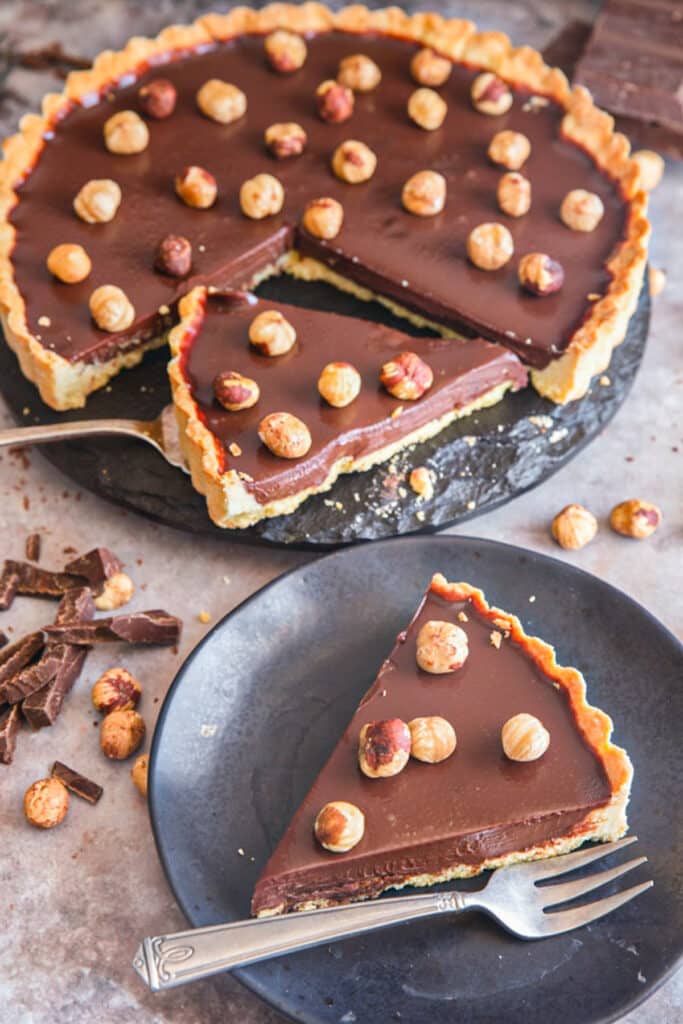 Chocolate crostata on a pie plate and a slice on a black plate.