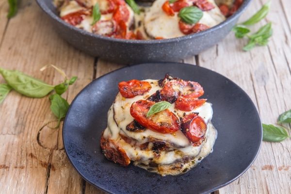 eggplant parmesan stacks in a pan and one on a black plate