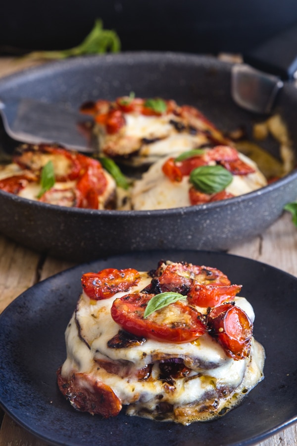 eggplant parmesan stacks in a pan and one on a black plate