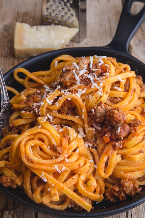 bolognese sauce with pasta and a sprinkle of parmesan cheese in a black pan