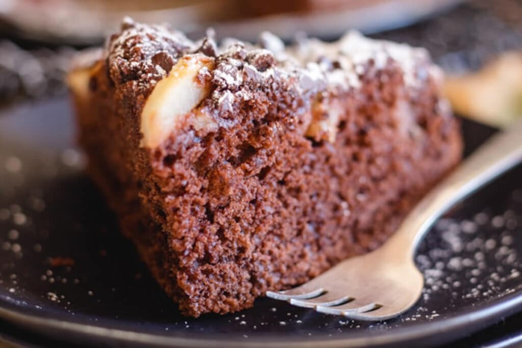 A slice of chocolate pear cake on a black plate.